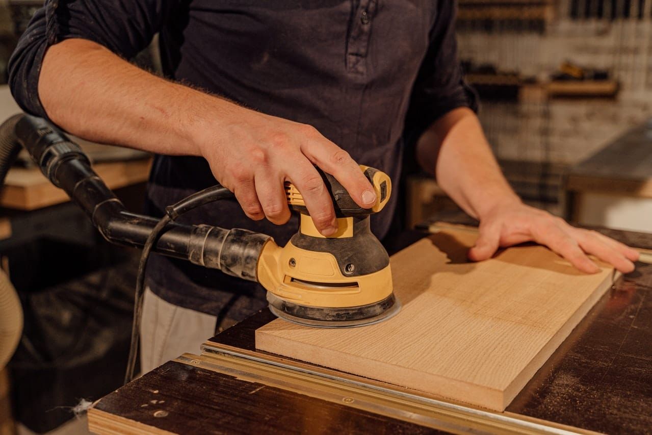 man using hand sander on a board